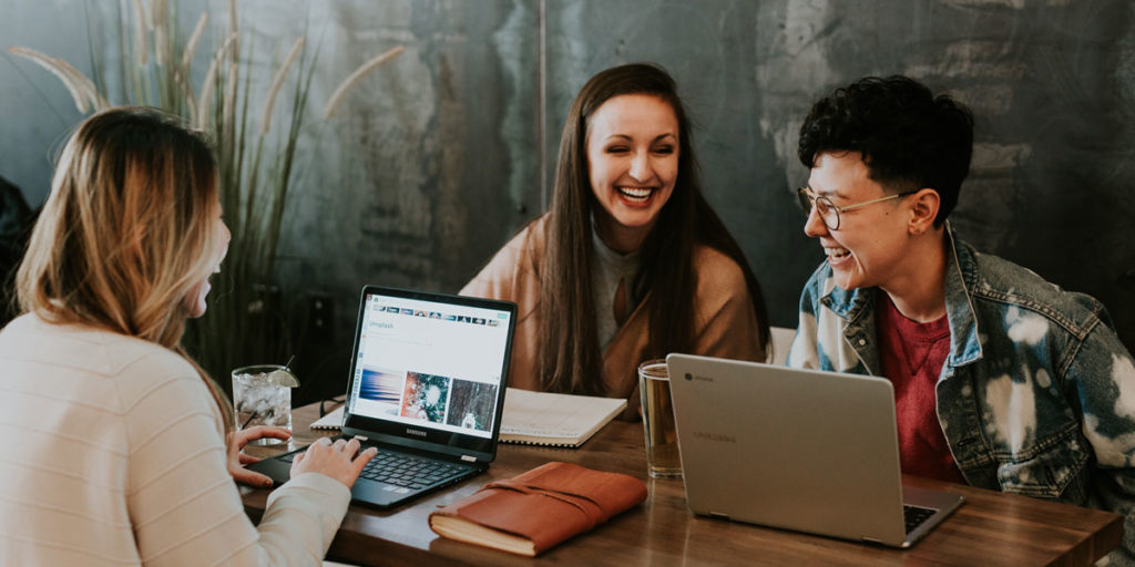 LC: Amigos rindo em uma mesa, mexendo em seus computadores.